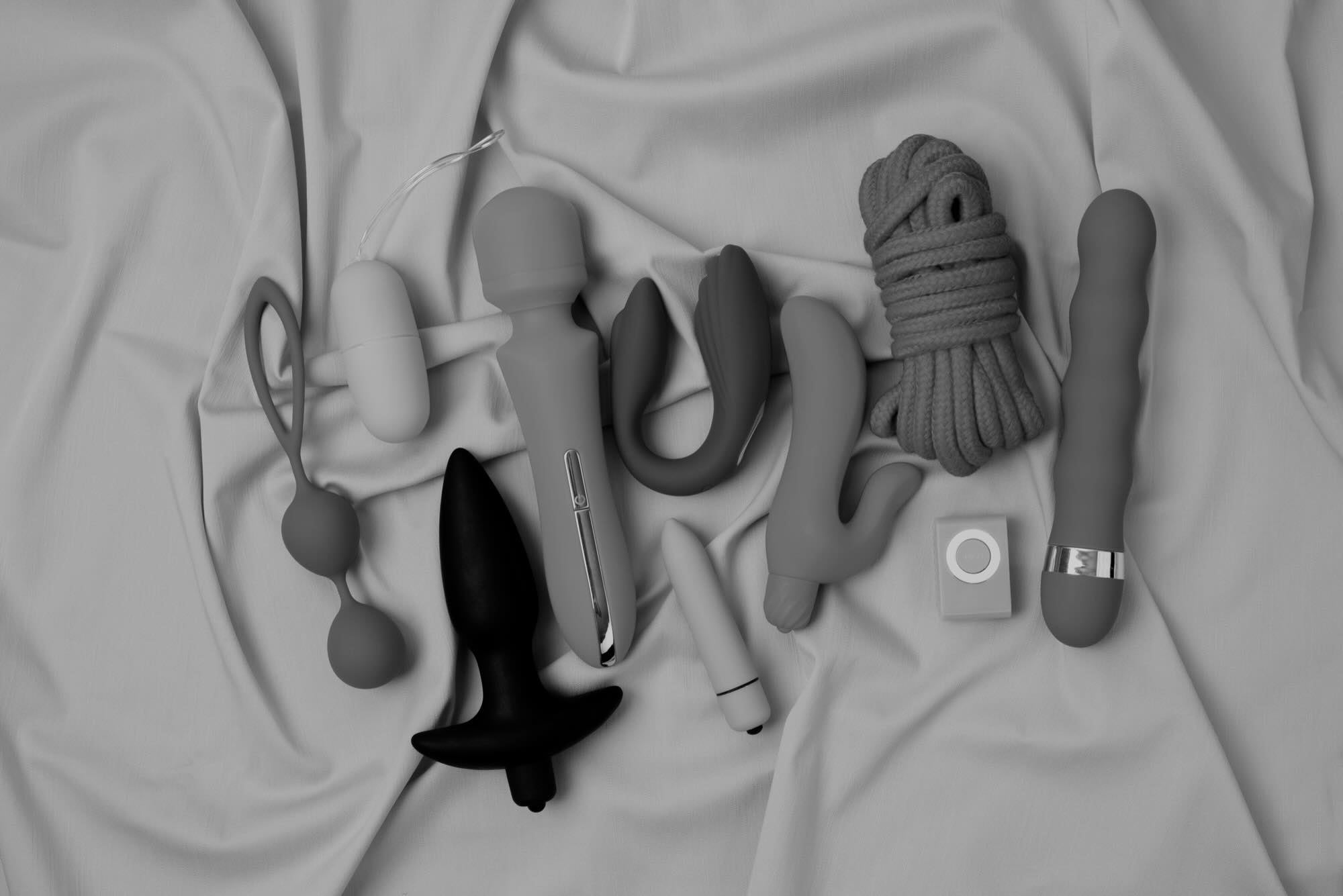 Various adult toys and sexy adult toys on a silk sheet.