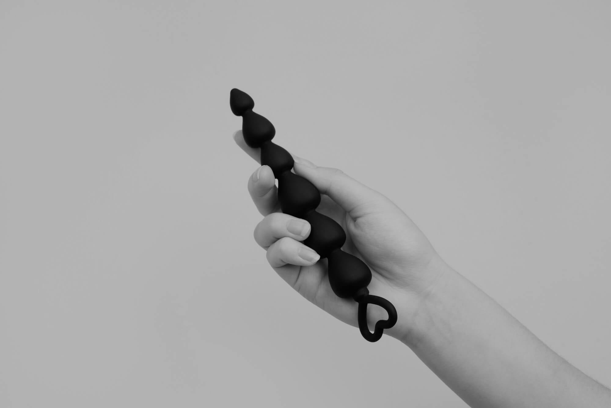 A woman holding a black beaded anal toy