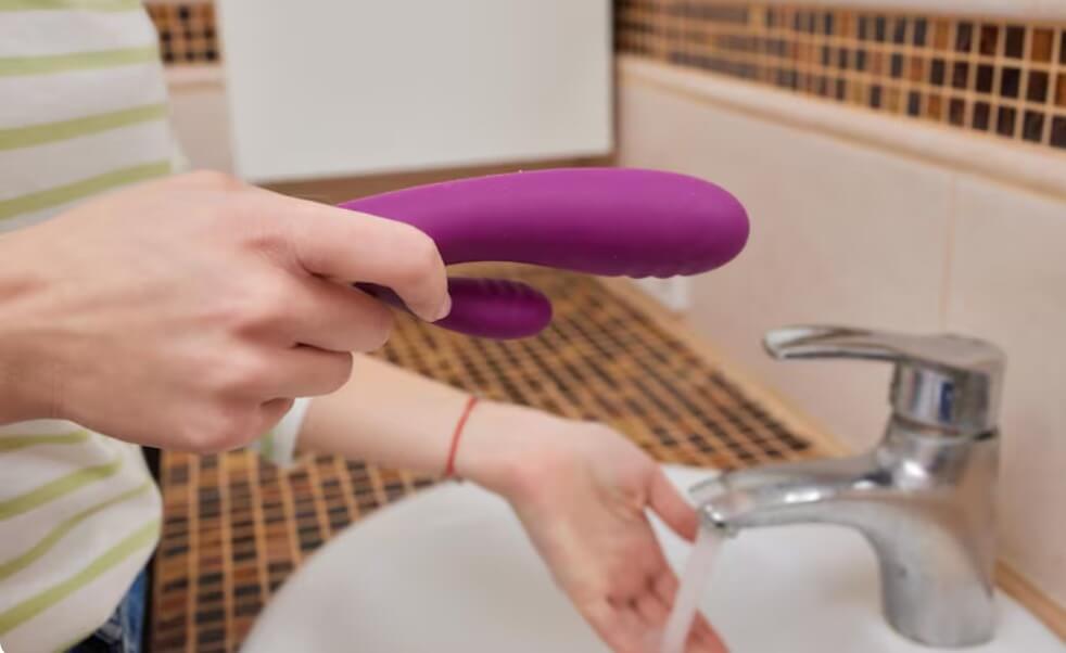 Young woman washes a sex toy in the sink at home