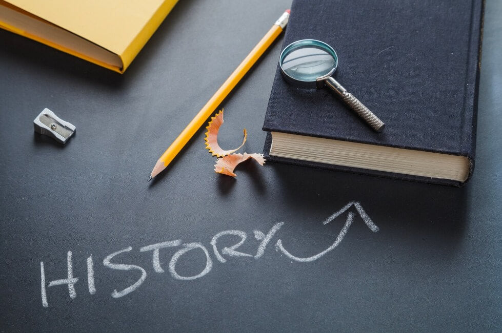 Magnifying glass and pencil beside the word history — exploring historical research and academic study.