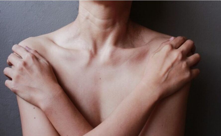 Close-up of a person crossing their arms over their shoulders against a neutral background.