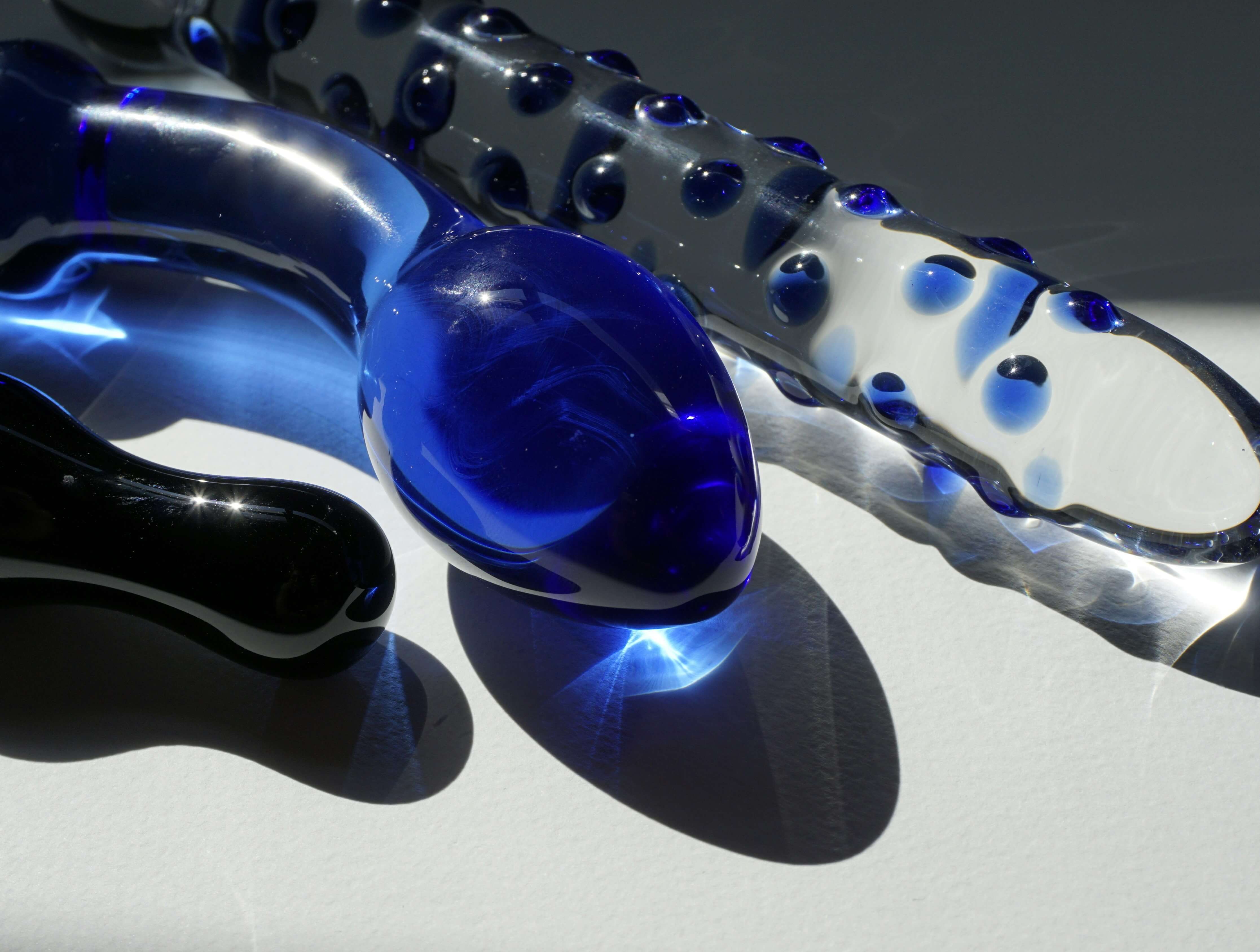 Shiny blue and clear glass dildos placed under natural light, illustrating how to clean glass dildo safely and maintain hygiene.
