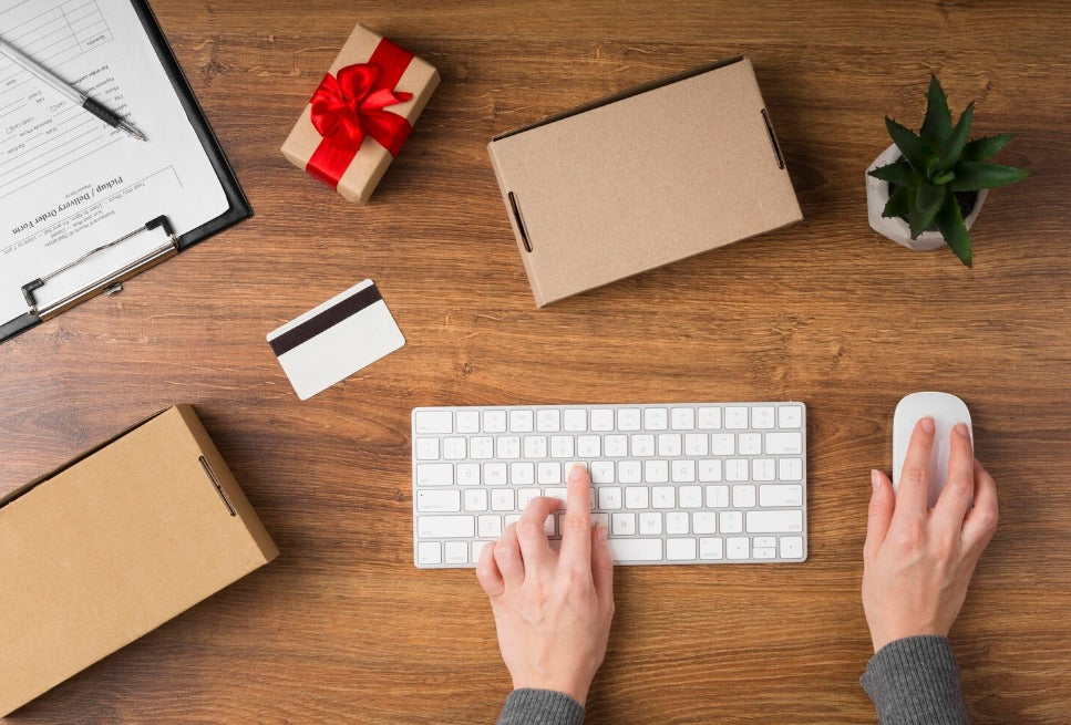 Person shopping online with keyboard and credit card, surrounded by discreet plain shipping boxes, highlighting privacy and safe package delivery.