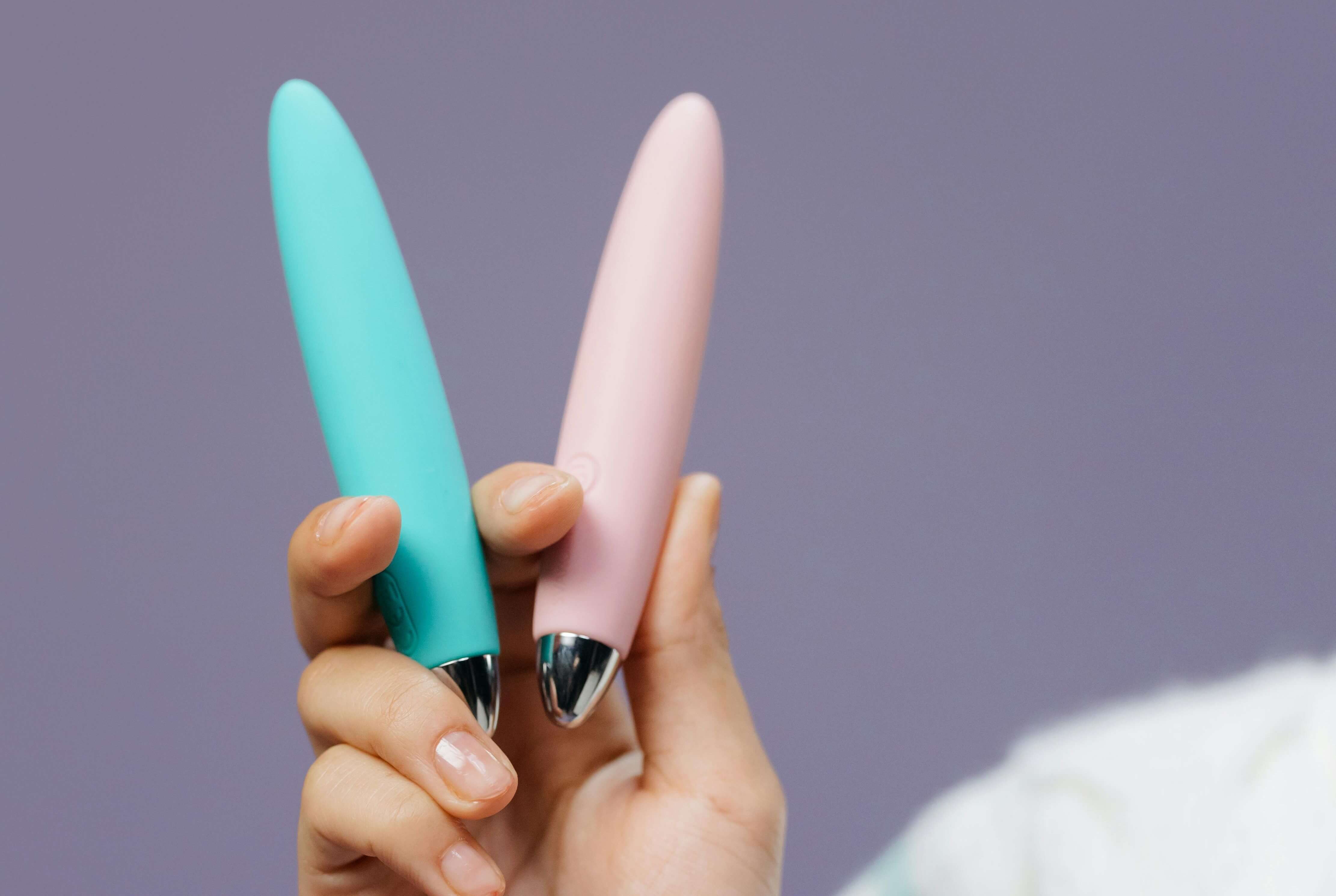 Hand holding pink and blue bullet vibrators used as compact personal massagers for stimulation.