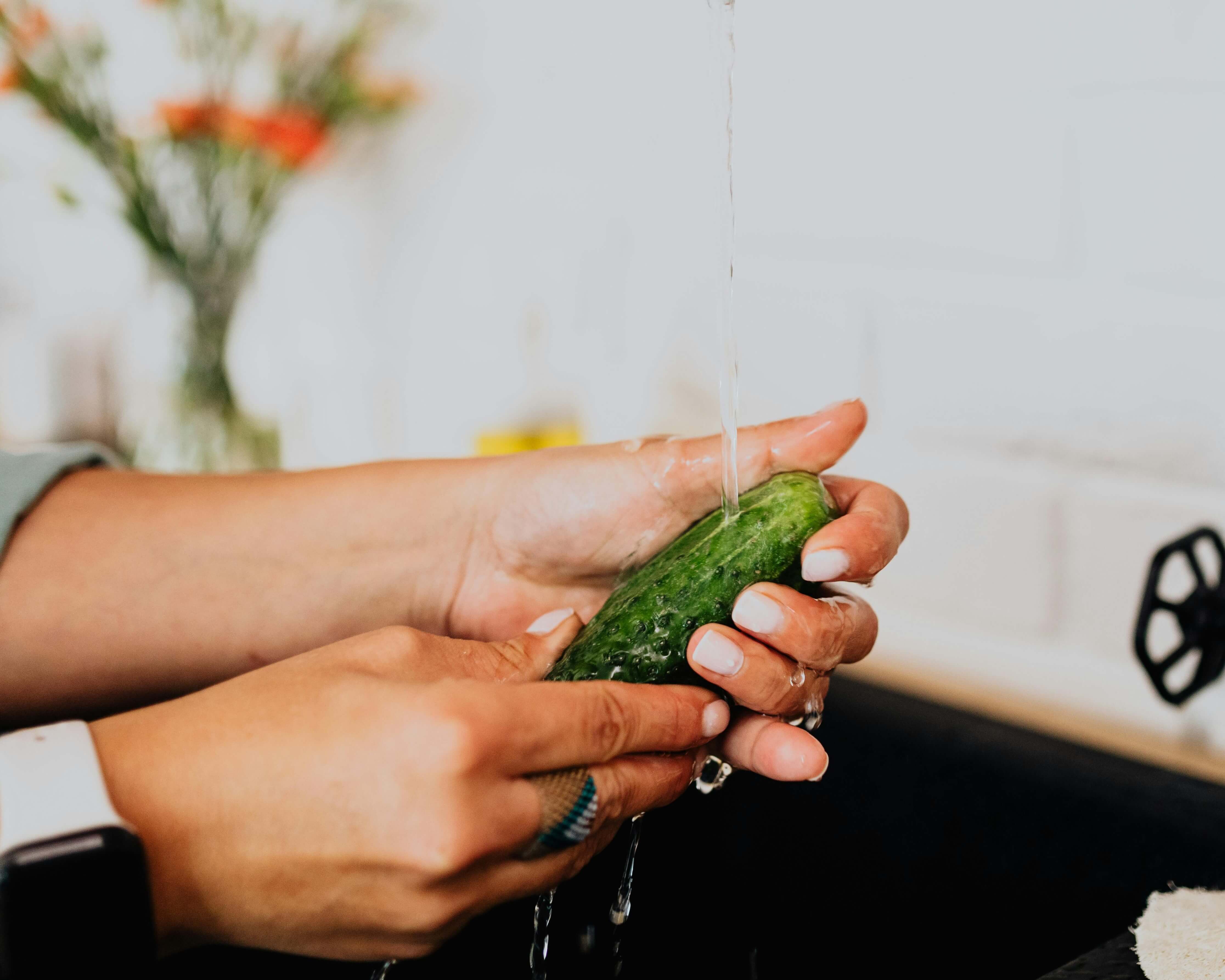 Running water over a cucumber as an analogy for cleaning an anal dildo safely and effectively.