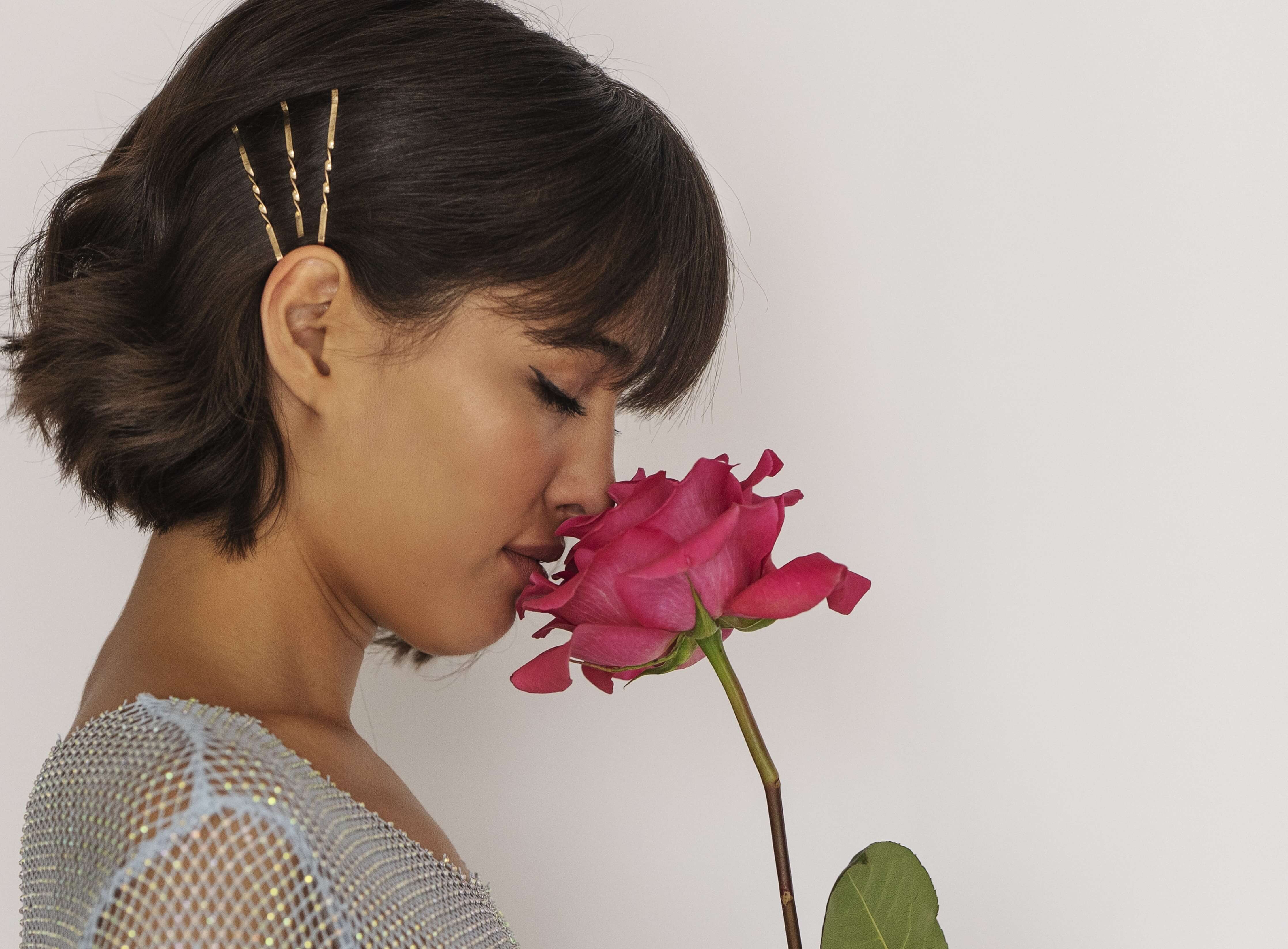 Side view of a woman enjoying a clean, pleasant scent from a pink rose representing freshness and effective ways to eliminate silicone dildo odors.