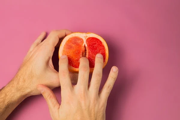 Male hand mimicing the action of clitoral sucking toys on a grapefruit. 