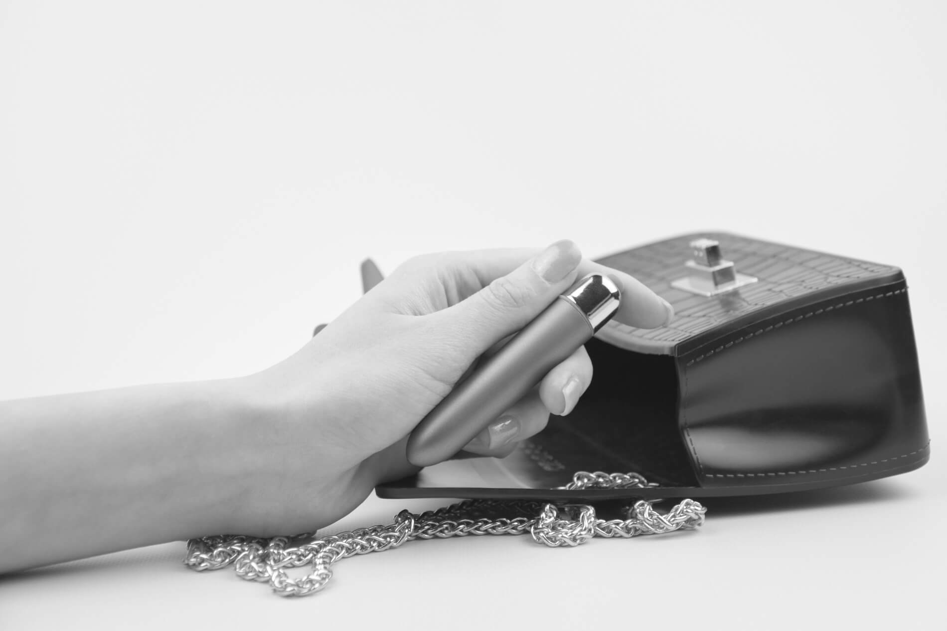 Woman holding a small vibrator from our small vibrators collection with a black purse in the background