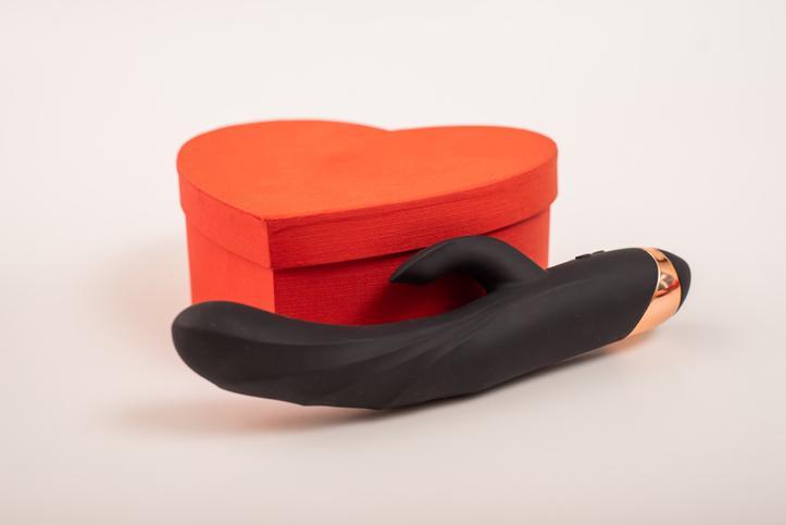 A black dildo next to a red heart shaped box