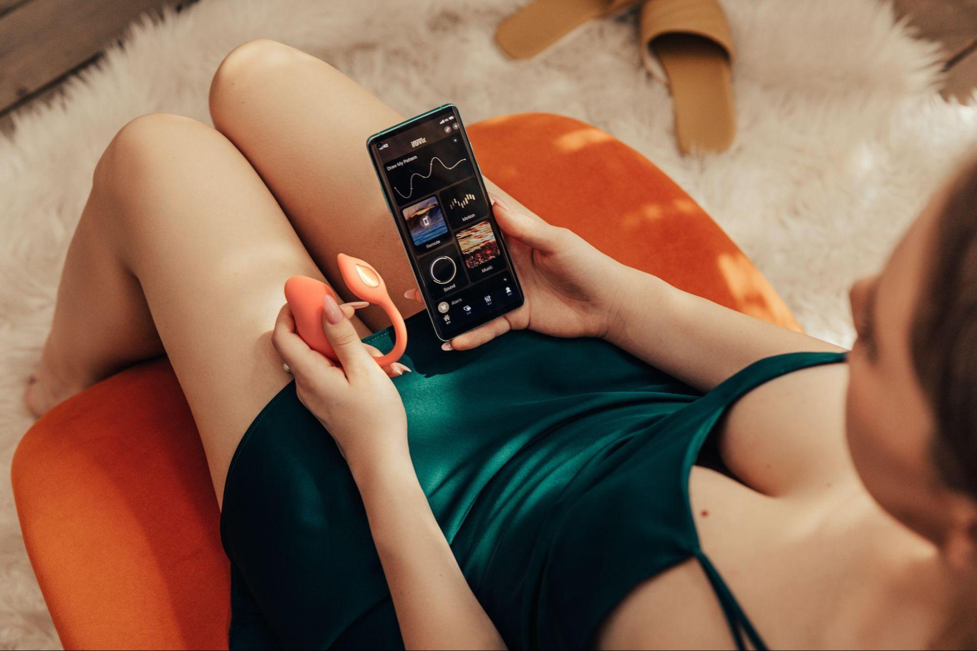 Woman sitting with a vibrator in one hand and a phone in the other