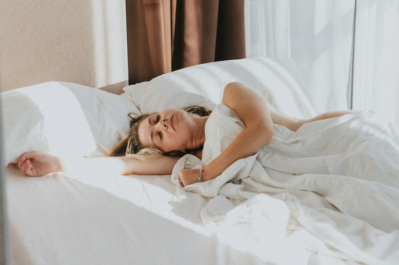 Woman relaxing comfortably in white bed linens