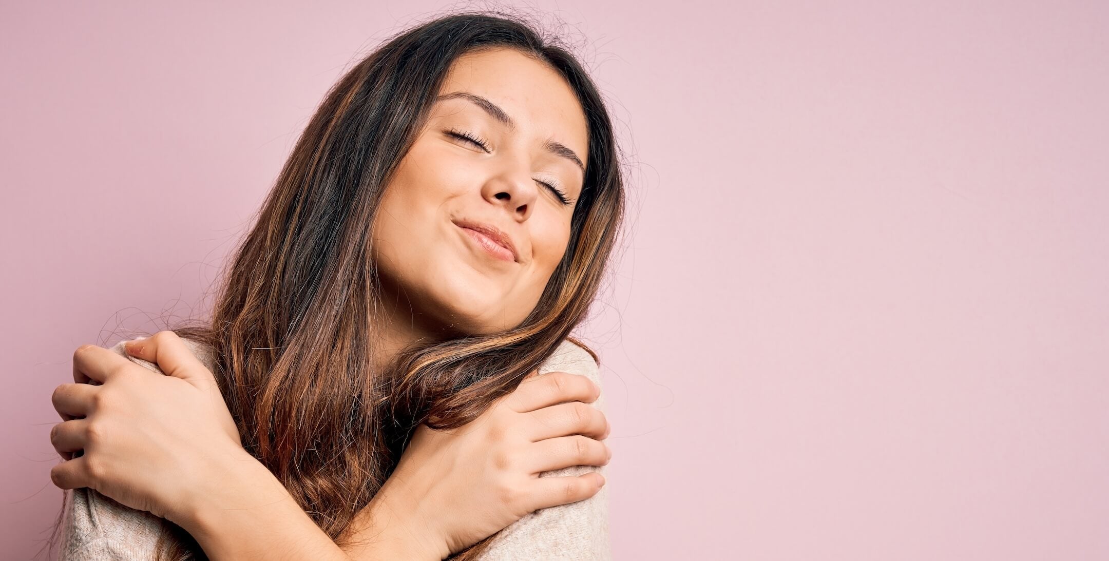 Woman hugging herself for self-love on a pink background after shopping at ThatMood adult toy store.